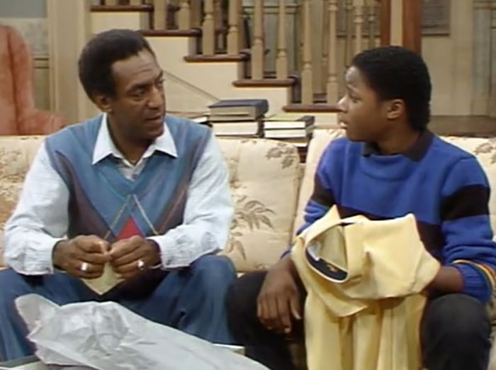 Bill Cosby and Malcolm-Jamal Warner sitting on a couch in a scene from The Cosby Show discussing family matters. - 12