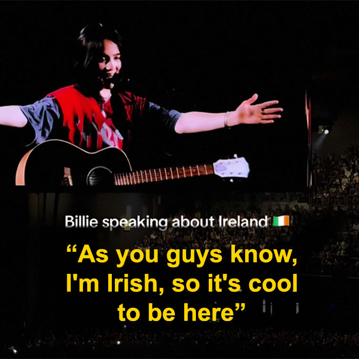 Billie Eilish performing on stage with a guitar, speaking during her Ireland show amid racism controversy.
