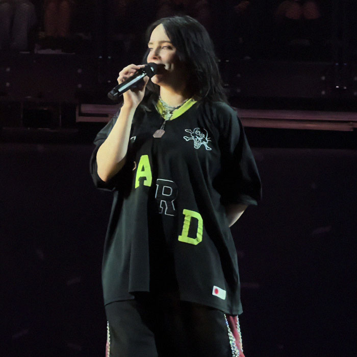 Billie Eilish performing on stage at a concert, holding a microphone during her Ireland show controversy.