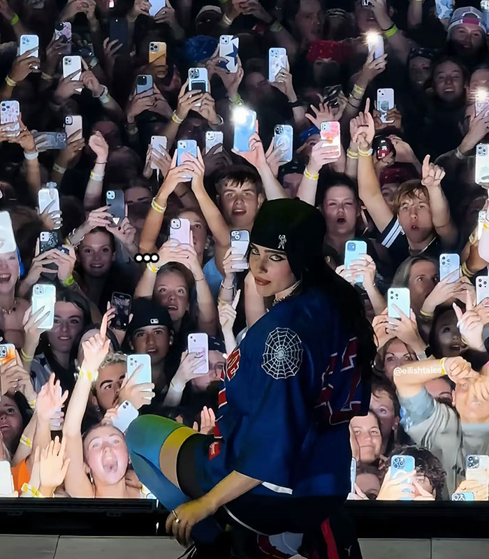 Billie Eilish performing on stage with fans holding up phones during concert amid controversy over comment in Ireland.
