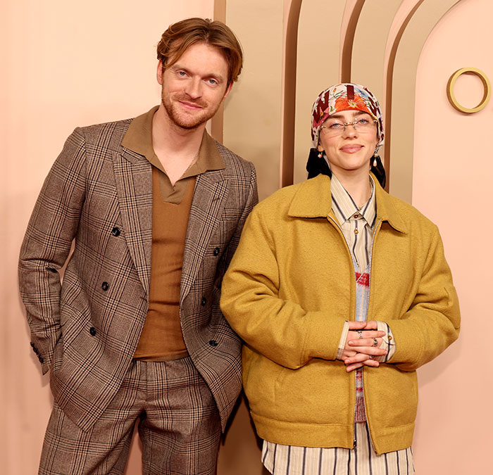 Billie Eilish at an event with a male companion, both dressed stylishly, amid media coverage on her Ireland show controversy.