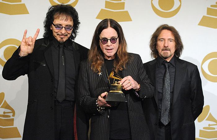 Black Sabbath band members posing at an event, with one holding a Grammy award in a formal setting.