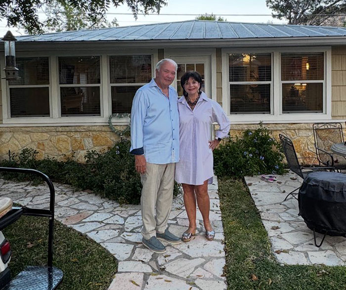 Older couple standing outside a house with a stone patio, related to sisters found with hands locked together in Texas floods.