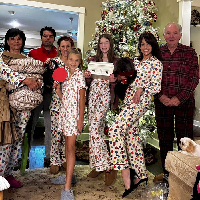 Family in colorful pajamas gathered by a decorated Christmas tree, representing sisters lost in Texas floods with hands locked together.