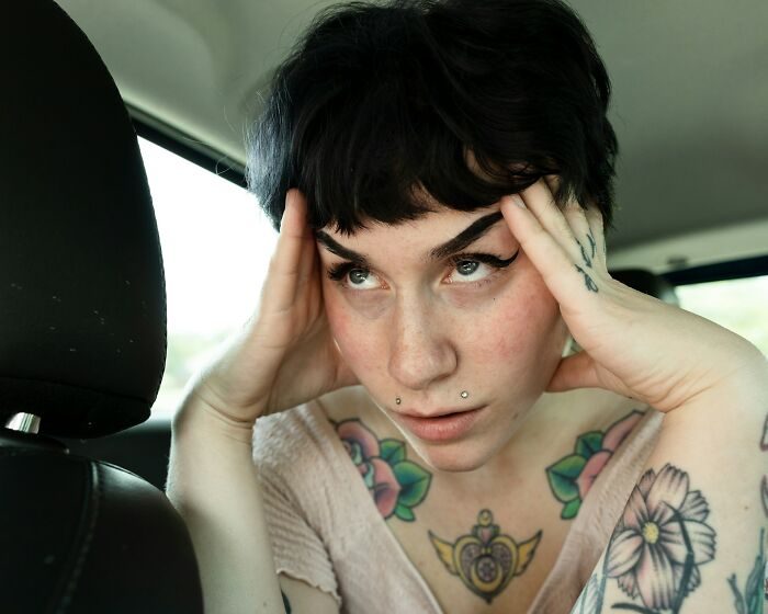 Young woman with tattoos and piercings in a car, showing frustration and stress answering unattractive traits in men.