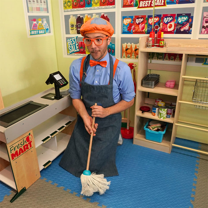 Blippi in colorful outfit mopping floor inside a play store, illustrating Blippi net worth and kids content gold rush. - 1