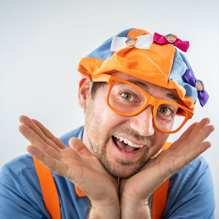 Man dressed as Blippi with bright orange glasses and hat, smiling, representing Blippi net worth and kids content growth. - 6