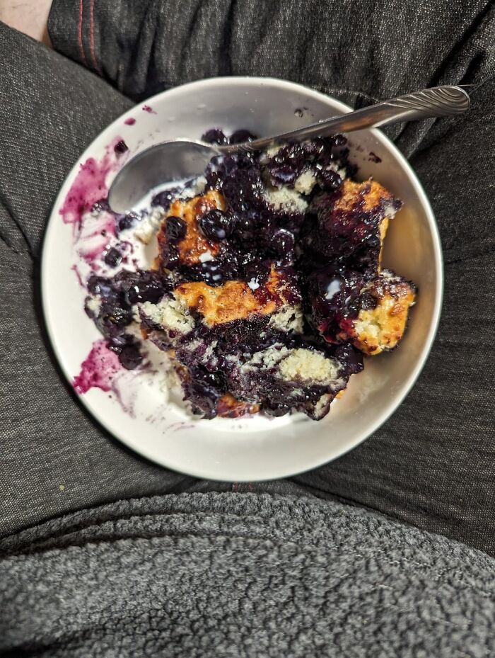 Bowl of blueberry cobbler with cream held on lap showing a surprising thing travelers share about the U.S.