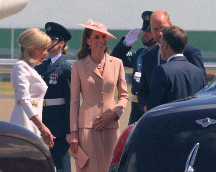 Brigitte Macron wearing white dress beside husband Emmanuel Macron during UK visit amid cold behavior claims.