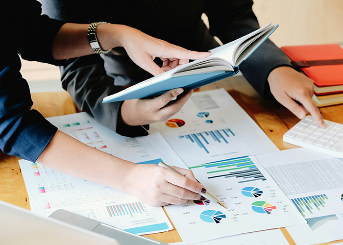Two colleagues analyzing charts and data reports at a desk, discussing data fudge to improve department results.