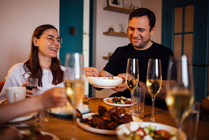 Man looking hungover and uncomfortable while having lunch with his girlfriend and her parents at a home dinner party.