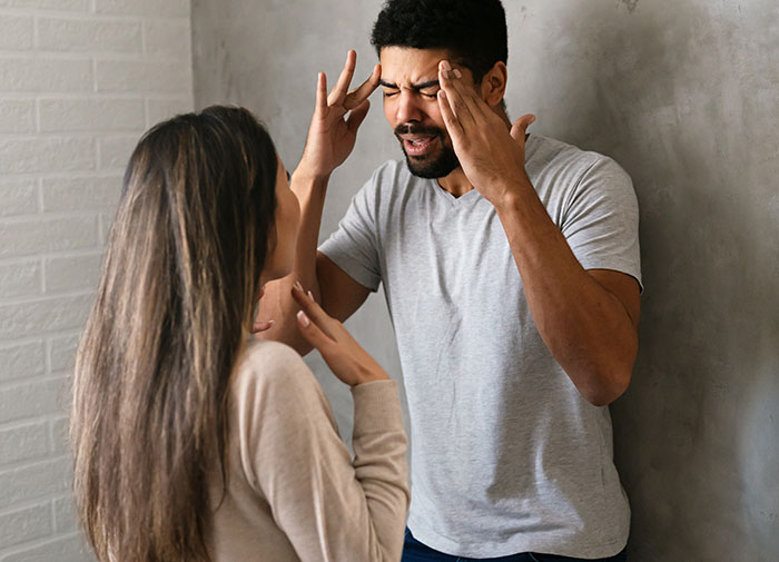 Man holding his head in pain, looking hungover while talking to a woman before meeting his girlfriend&rsquo;s parents.
