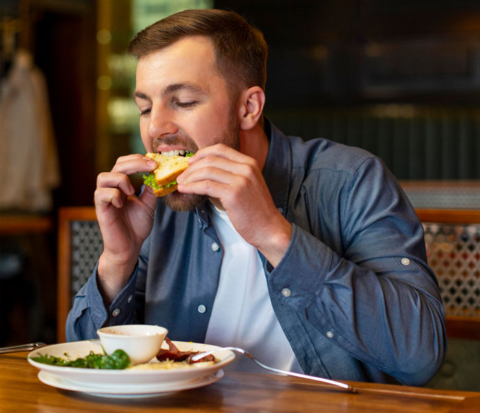 Man eating a sandwich at a restaurant, representing the guy nagging his girlfriend to eat more in the relationship story.