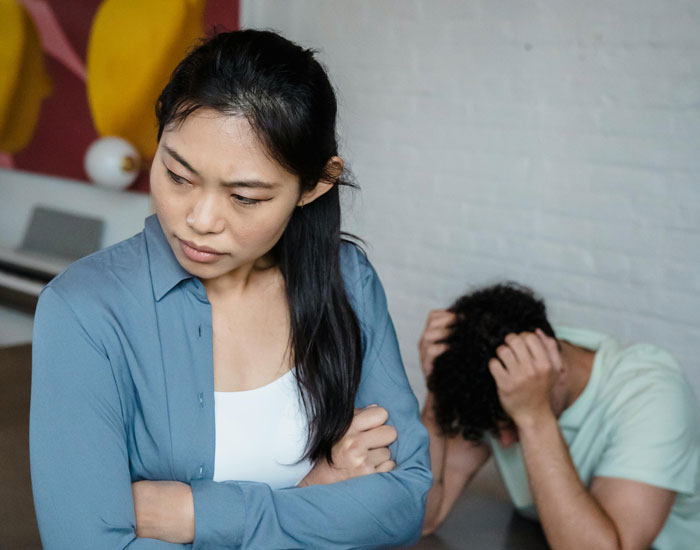 Upset couple in disagreement, woman crossing arms looking away while man holds his head in frustration indoors.