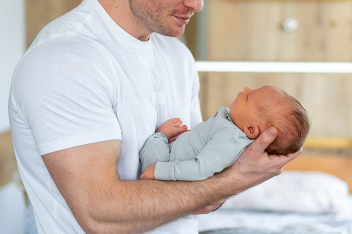 Man holding his newborn daughter in arms at home, highlighting cycle trip choice over watching his child. Man holding his newborn daughter in arms at home, highlighting cycle trip choice over watching his child.