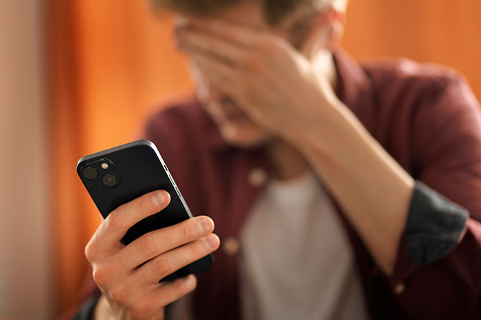 Person covering face in frustration while looking at phone, reflecting on friends who were actually total jerks.