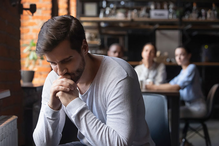 Man looking thoughtful and upset while friends sit and chat in the background, reflecting on people who noticed jerk friends.