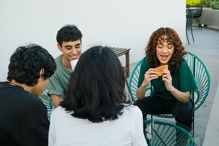 Group of young people sitting outdoors, sharing food and drinks, capturing moments of friendship and connection.