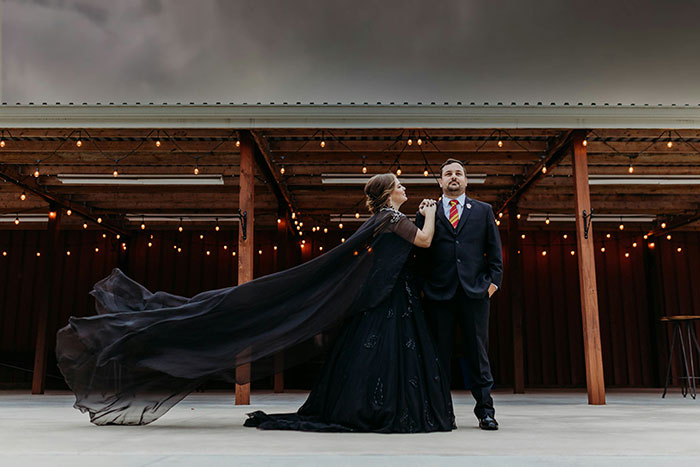 Bride in flowing black dress and fiancé in suit pose under string lights, reflecting tension with fiancé’s female friend demands. - 5