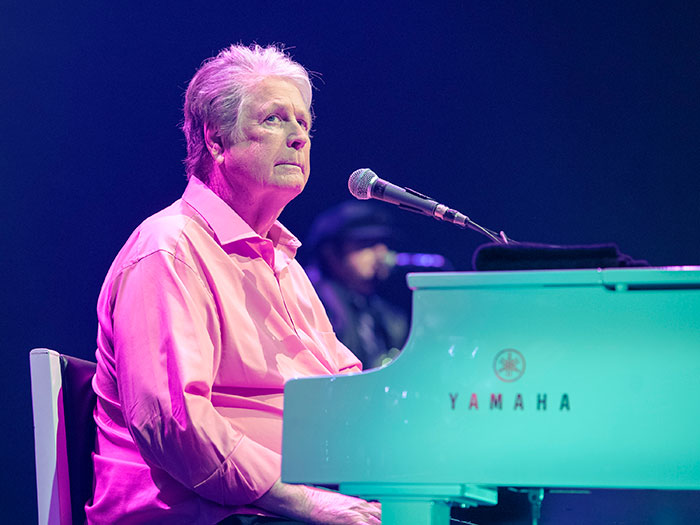 Elderly musician playing a Yamaha piano on stage, representing stars we've lost this year in July.