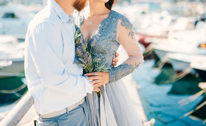 Couple embracing near boats, woman in lace dress holding flowers, capturing moment related to bride and unexpected dog grooming. - 21