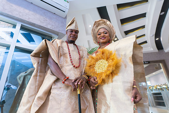 Bride and groom dressed in traditional attire, posing indoors with a bright smile, representing bride sister steal money caught camera.