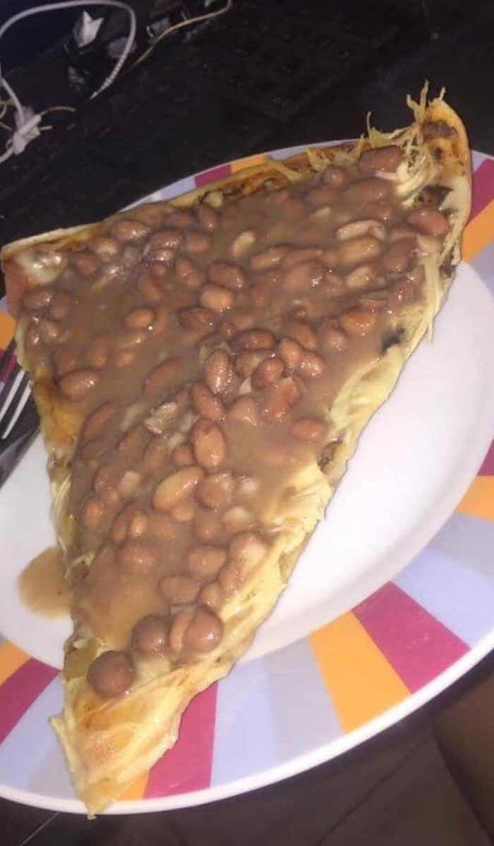 Slice of pizza topped with baked beans on a colorful plate, a funny meme about life in the UK food culture.