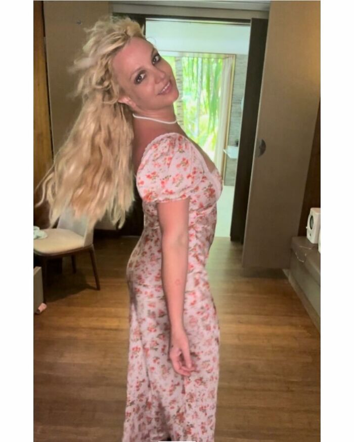 Britney Spears smiling indoors wearing a floral dress, sparking frenzy after announcing adoption of a baby girl.