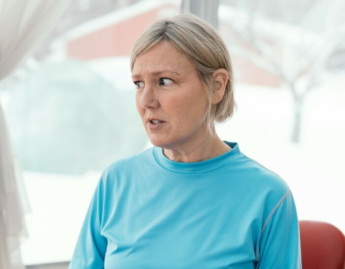 Middle-aged woman in a blue shirt looking away thoughtfully, reflecting on what makes a man instantly unattractive to women.