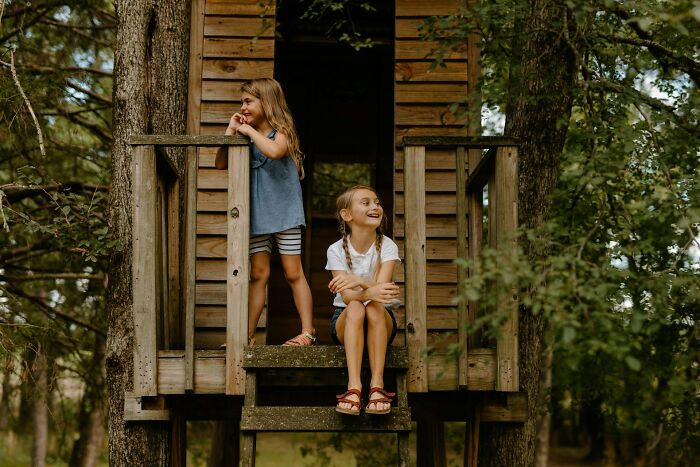 Two young girls enjoying time outside on a wooden treehouse, representing daily wins from feminists.