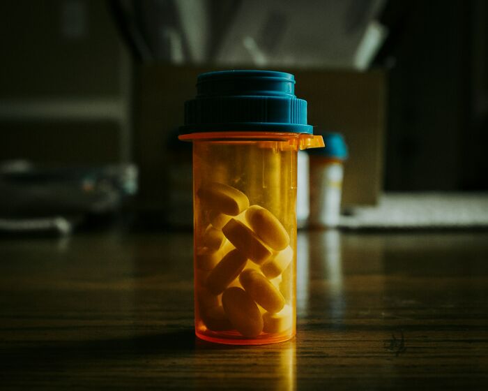 Amber prescription bottle filled with yellow pills on a wooden table, highlighting medical items found on patients.