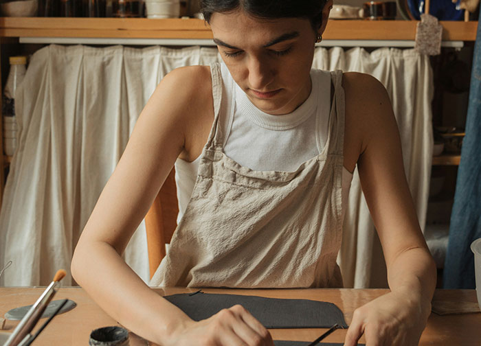Young woman focused on painting pottery at a wooden table, highlighting men's brutal honesty and personal expression. - 29