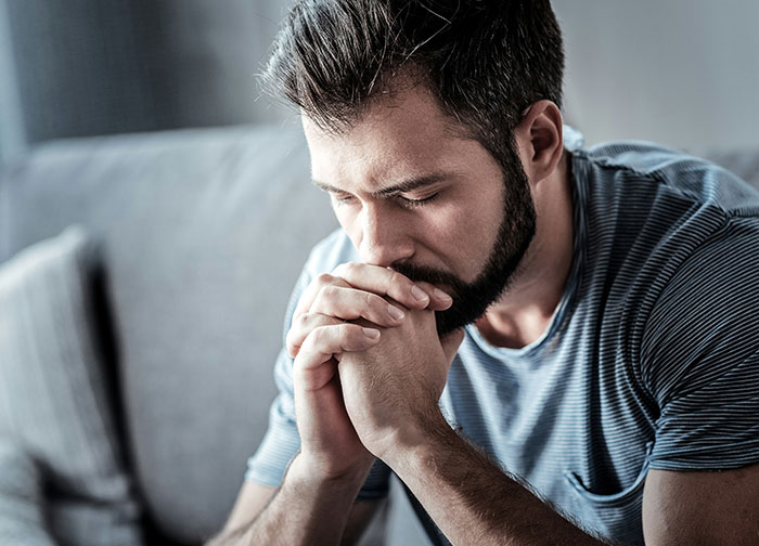 A man with a beard sitting on a couch looking thoughtful and stressed, illustrating men get brutally honest moments. - 5
