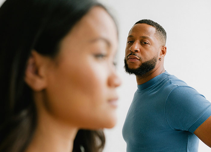 Man with beard looking seriously towards the camera while woman in foreground is out of focus, depicting brutal honesty theme. - 37