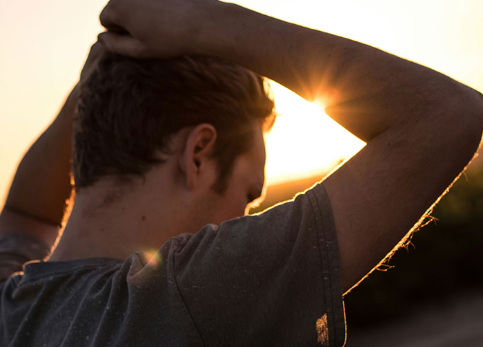 Young man looking away with hands on head at sunset, reflecting on honesty and emotions men rarely reveal. - 10