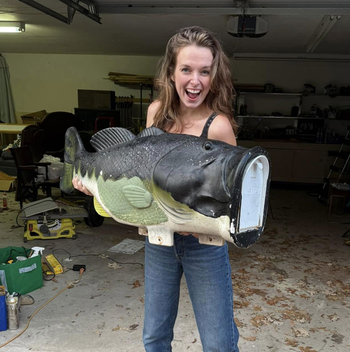 Woman holding a large novelty fish mailbox, illustrating curiosity about AI products and their unexpected designs.