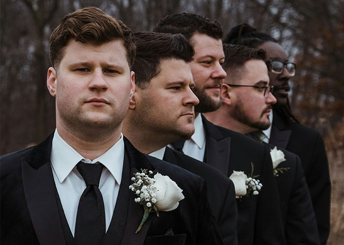 Group of men in tuxedos with white rose boutonnieres standing outdoors, illustrating call off wedding weird family tradition.