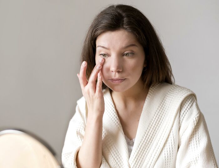 Woman in a white robe examines her eye closely, illustrating cancer symptoms in a personal doctor story setting.