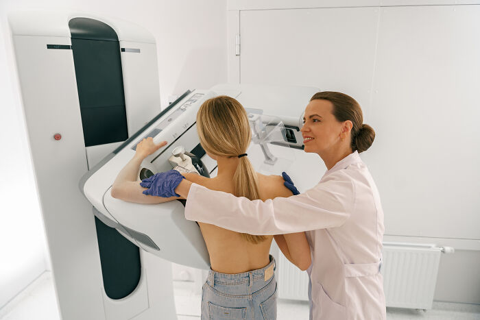 Doctor assisting patient with breast cancer symptoms screening using a mammogram machine in a clinical setting.