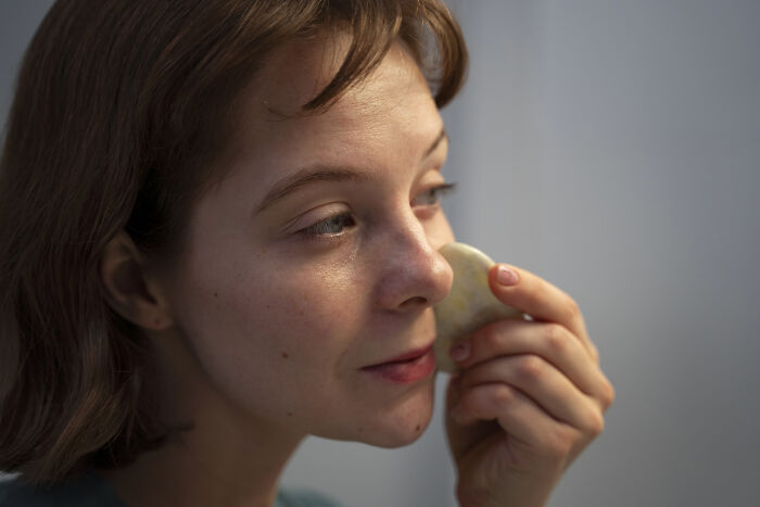 Woman using a facial stone tool, showing subtle signs of skin changes related to cancer symptoms in a calm setting.