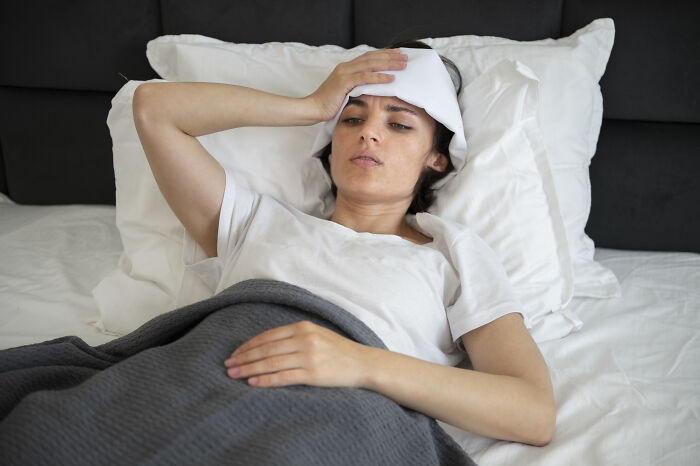 Woman lying in bed with a cold compress on her forehead, showing possible cancer symptoms in a doctor story context.