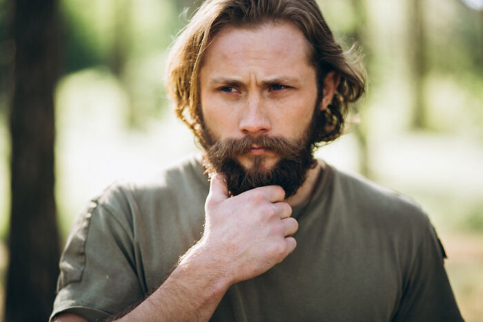 Man with beard and long hair outdoors, looking thoughtful while reflecting on cancer symptoms and doctor stories.