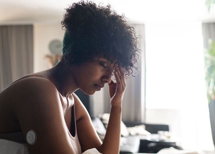 Woman sitting with eyes closed and hand on forehead, showing cancer symptoms and concern in a quiet room.