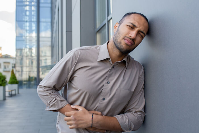 Man in a brown shirt leaning against a wall, showing discomfort and pain, illustrating cancer symptoms in doctor stories.