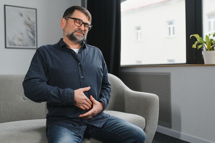 Middle-aged man sitting on a couch holding his stomach in pain, illustrating cancer symptoms doctor stories.