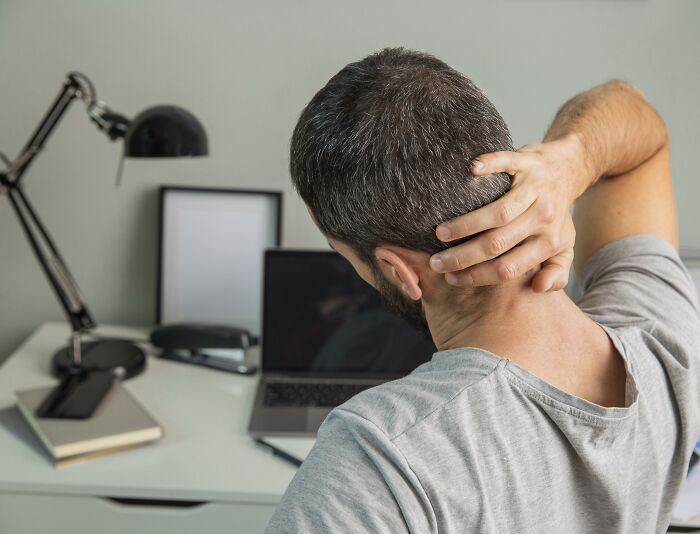 Man holding neck in discomfort while sitting at a desk with laptop, illustrating cancer symptoms doctor stories concept.