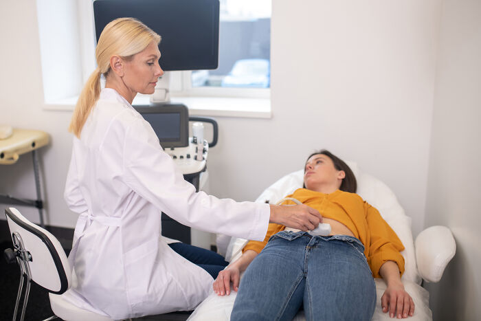 Female doctor performing an abdominal ultrasound on a patient in a clinic, focusing on cancer symptoms and doctor stories.