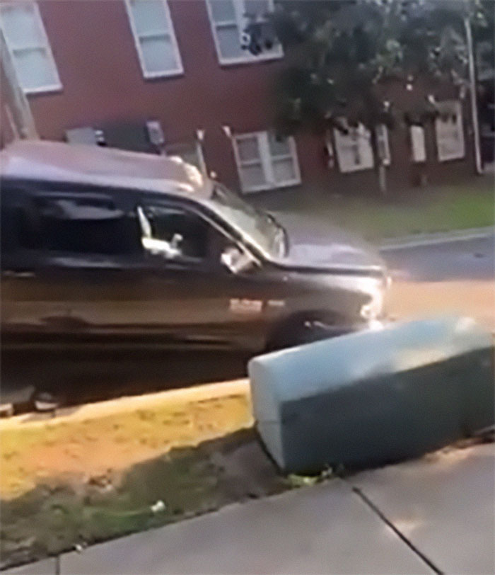 Black truck approaching a sinkhole on a residential street after a warning was ignored due to racism incident.