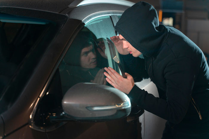 Car thieves in hooded sweatshirt trying to break into a car at night through the window, reflecting in the glass. - 4