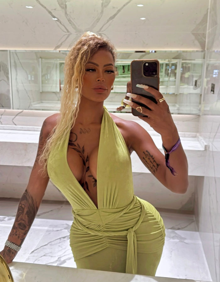 Woman taking a mirror selfie in a green dress, showcasing tattoos and confident pose after butt surgery journey. - 2